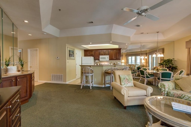 carpeted living room with a raised ceiling and ceiling fan with notable chandelier