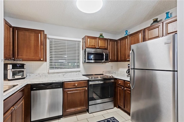 kitchen with stainless steel appliances, tasteful backsplash, light tile patterned floors, and a textured ceiling