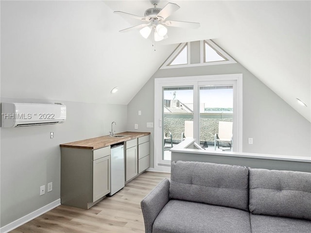 kitchen with lofted ceiling, sink, butcher block countertops, an AC wall unit, and light hardwood / wood-style floors