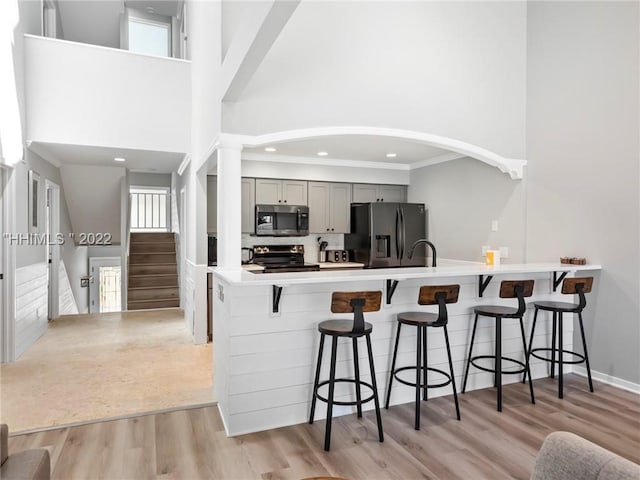 kitchen with gray cabinetry, stainless steel appliances, light hardwood / wood-style floors, a kitchen bar, and decorative backsplash