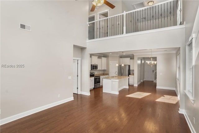 unfurnished living room featuring a high ceiling, sink, dark wood-type flooring, and ceiling fan with notable chandelier