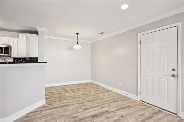 interior space with white cabinetry, ornamental molding, decorative light fixtures, and light wood-type flooring