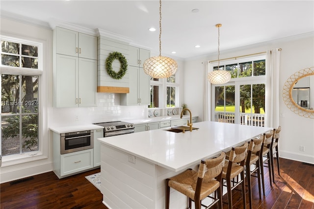 kitchen featuring crown molding, appliances with stainless steel finishes, dark hardwood / wood-style flooring, pendant lighting, and a kitchen island with sink