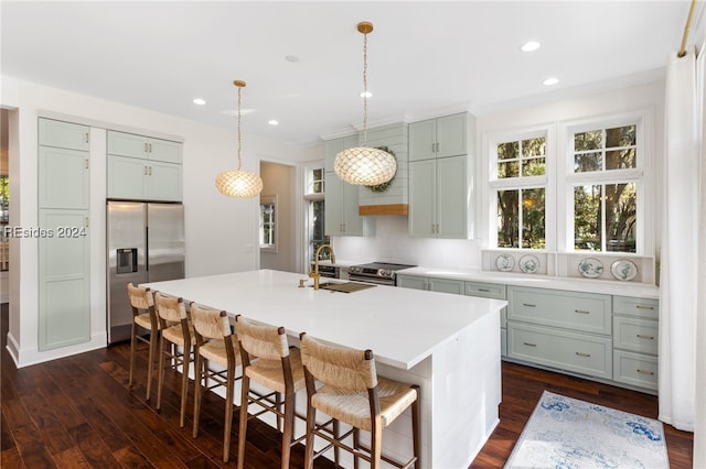 kitchen featuring dark wood-type flooring, appliances with stainless steel finishes, a kitchen breakfast bar, a center island with sink, and decorative light fixtures