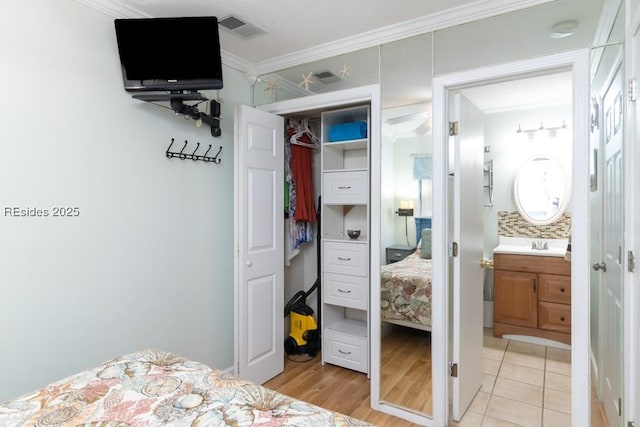 tiled bedroom with ornamental molding, ensuite bathroom, and sink