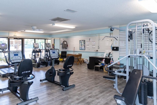 gym featuring hardwood / wood-style flooring, a textured ceiling, and ceiling fan