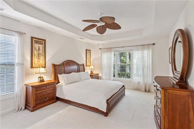 bedroom with a raised ceiling, light colored carpet, and ceiling fan