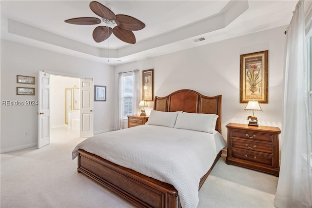 carpeted bedroom with a tray ceiling, ceiling fan, and ensuite bathroom