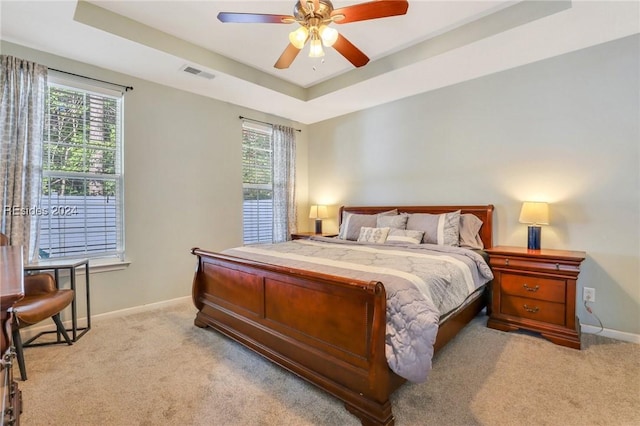 carpeted bedroom with multiple windows, a tray ceiling, and ceiling fan