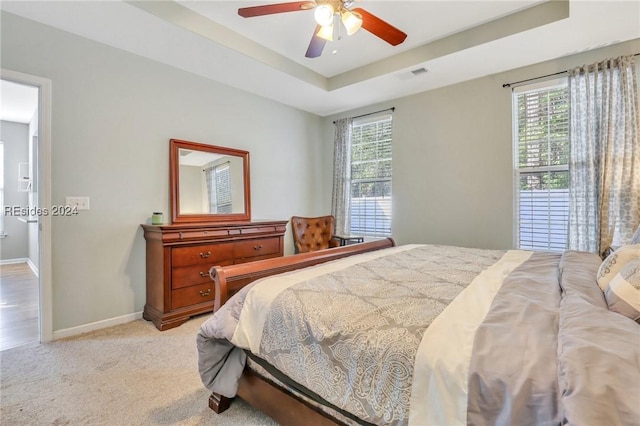 bedroom featuring light carpet, ceiling fan, and a tray ceiling