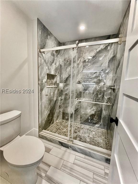 bathroom featuring a shower with shower door and toilet