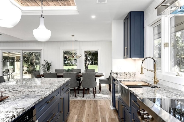 kitchen featuring pendant lighting, blue cabinets, light hardwood / wood-style floors, and light stone counters