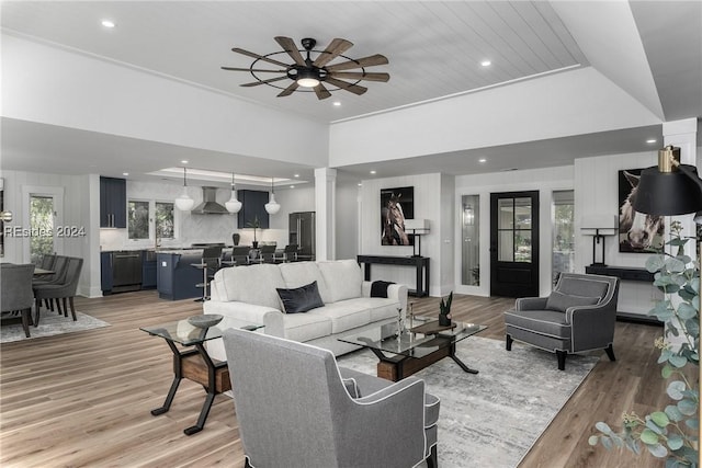 living room with crown molding, ceiling fan, light wood-type flooring, wooden ceiling, and ornate columns