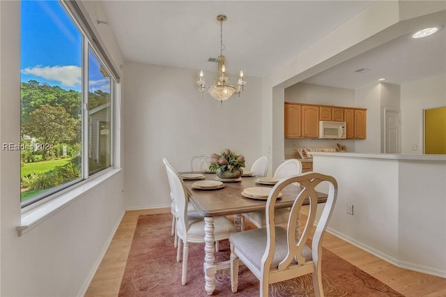 dining room with an inviting chandelier, a healthy amount of sunlight, and light hardwood / wood-style flooring