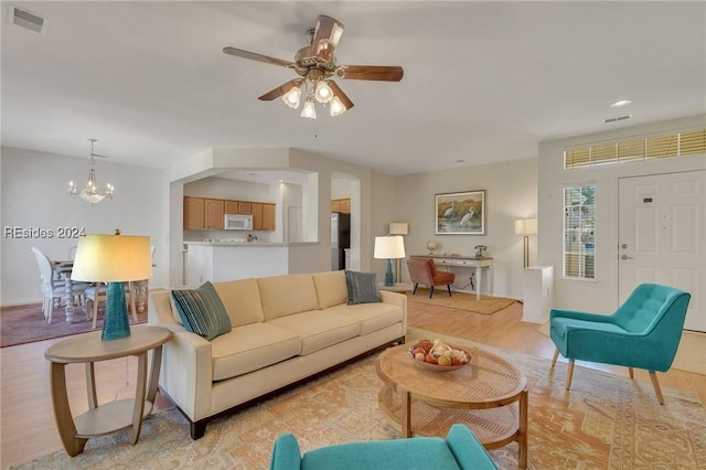 living room featuring ceiling fan with notable chandelier and light wood-type flooring