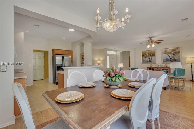 dining space with ceiling fan with notable chandelier and light wood-type flooring