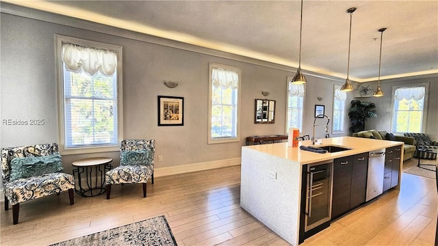 kitchen with sink, a kitchen island with sink, light hardwood / wood-style floors, decorative light fixtures, and beverage cooler