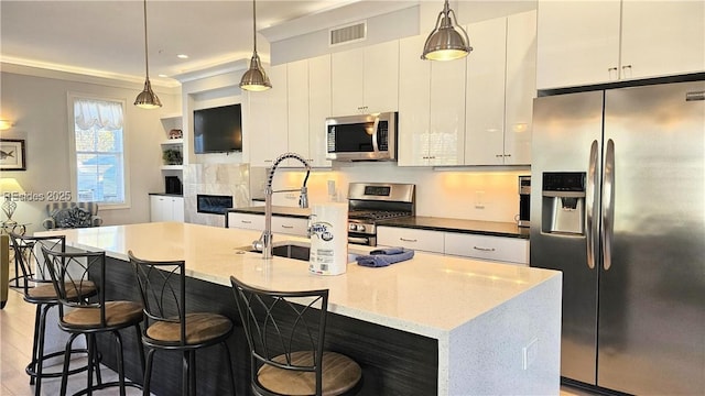 kitchen with stainless steel appliances, a kitchen island with sink, pendant lighting, and white cabinets