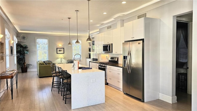 kitchen with appliances with stainless steel finishes, an island with sink, sink, white cabinets, and hanging light fixtures