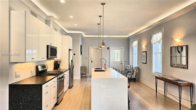 kitchen featuring sink, decorative light fixtures, appliances with stainless steel finishes, an island with sink, and white cabinets