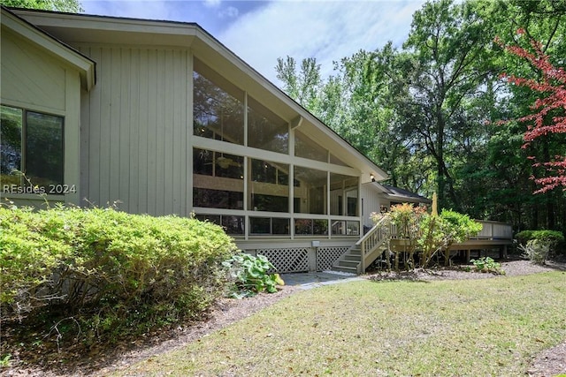 view of property exterior featuring a lawn, a sunroom, and a deck