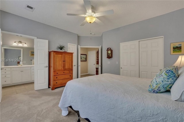 bedroom featuring ensuite bathroom, light colored carpet, a textured ceiling, a closet, and ceiling fan