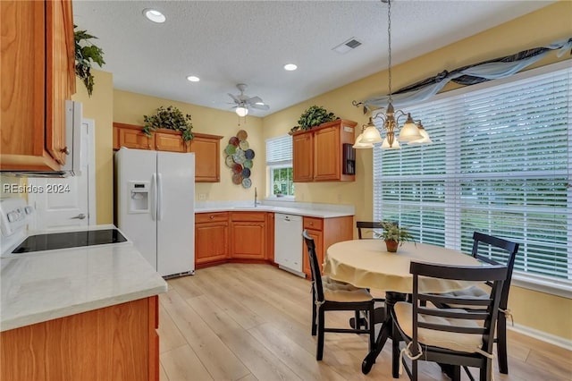 kitchen with sink, light wood-type flooring, hanging light fixtures, white appliances, and a textured ceiling