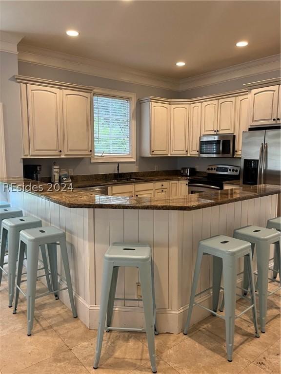 kitchen featuring dark stone countertops, a breakfast bar area, kitchen peninsula, and appliances with stainless steel finishes