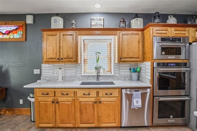 kitchen featuring tasteful backsplash, light stone countertops, appliances with stainless steel finishes, and sink