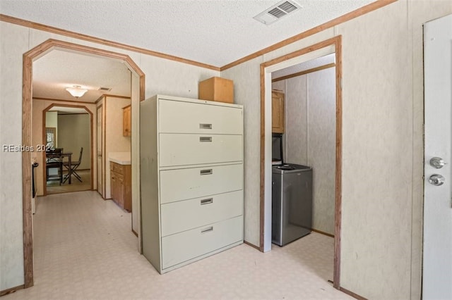 hallway featuring a textured ceiling, ornamental molding, and washing machine and clothes dryer