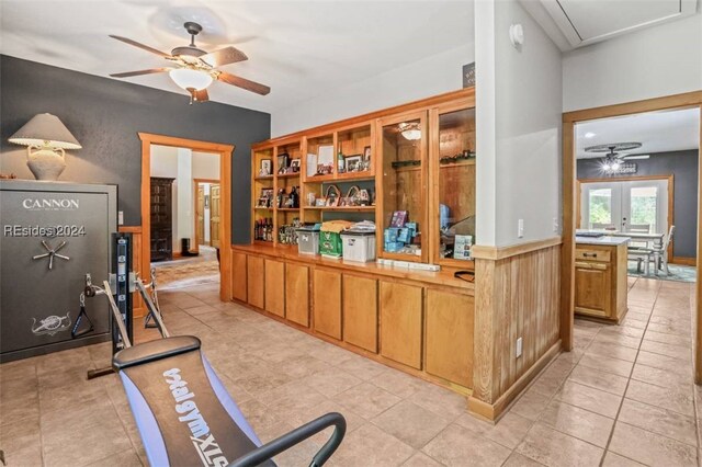 bar with light tile patterned flooring, ceiling fan, french doors, and wood walls