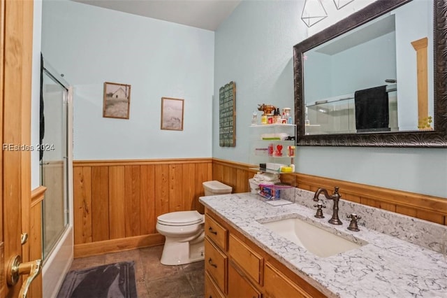 full bathroom featuring combined bath / shower with glass door, wood walls, tile patterned flooring, vanity, and toilet