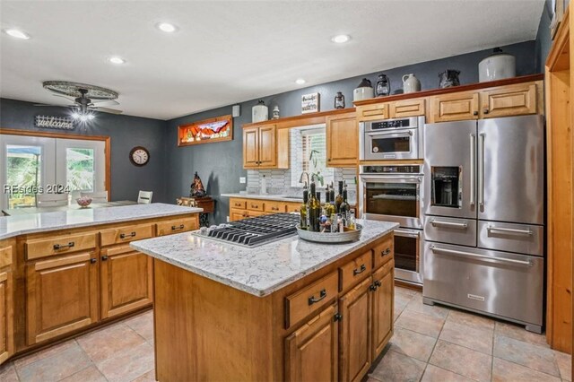 kitchen with a center island, appliances with stainless steel finishes, ceiling fan, light stone countertops, and decorative backsplash