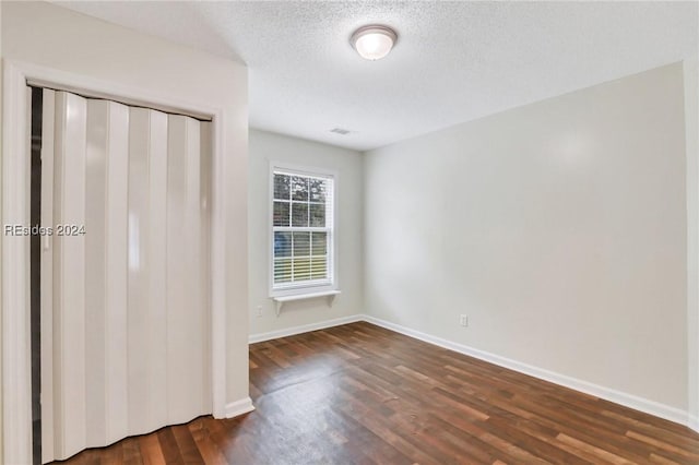 unfurnished bedroom featuring a textured ceiling, dark hardwood / wood-style flooring, and a closet