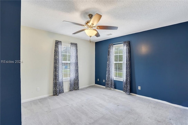 empty room featuring ceiling fan, a healthy amount of sunlight, light carpet, and a textured ceiling