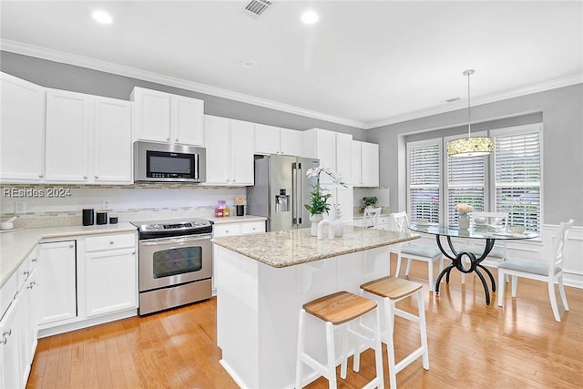 kitchen featuring a center island, ornamental molding, pendant lighting, stainless steel appliances, and white cabinets