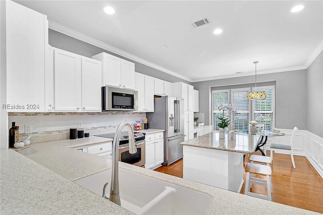 kitchen with stainless steel appliances, white cabinetry, hanging light fixtures, and crown molding