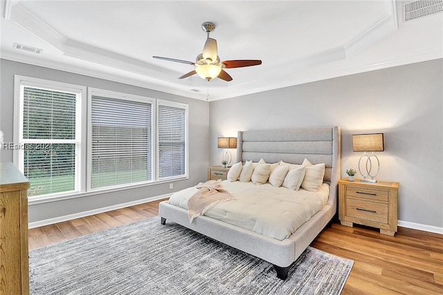 bedroom featuring a raised ceiling, ornamental molding, ceiling fan, and light hardwood / wood-style floors