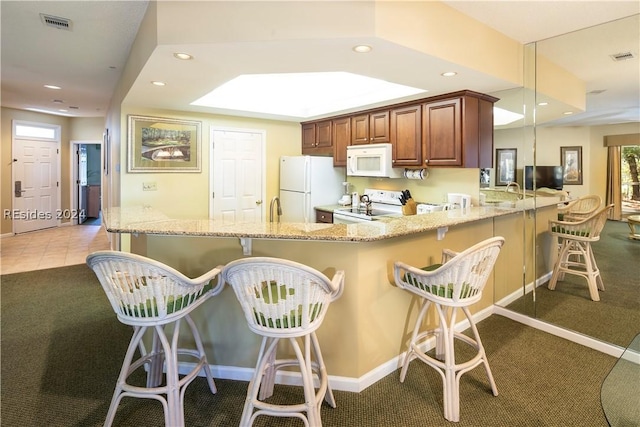 kitchen with dark carpet, decorative light fixtures, white appliances, and kitchen peninsula