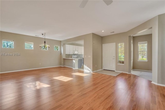 unfurnished living room featuring ceiling fan with notable chandelier and light hardwood / wood-style floors