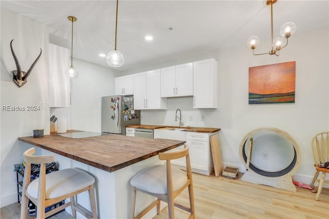 kitchen with butcher block countertops, appliances with stainless steel finishes, white cabinetry, hanging light fixtures, and a kitchen bar