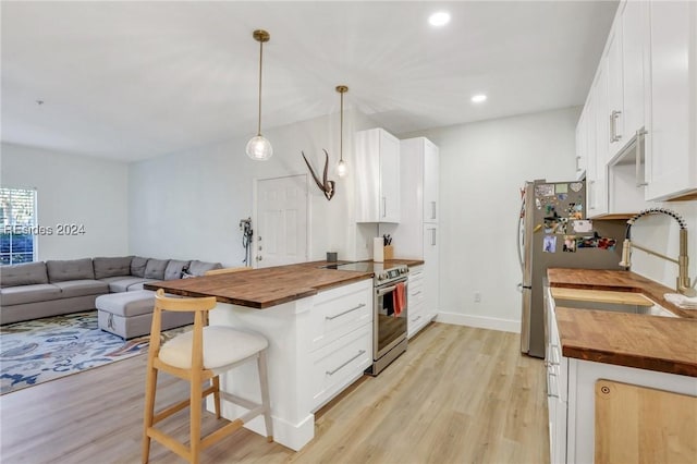 kitchen with stainless steel electric range oven, wooden counters, white cabinetry, a kitchen bar, and decorative light fixtures