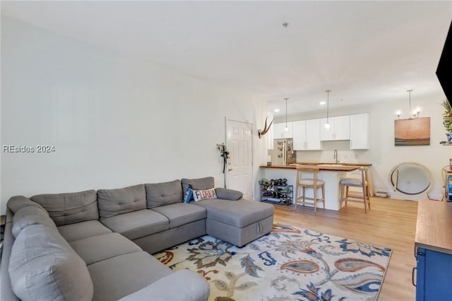 living room with an inviting chandelier, sink, and light wood-type flooring