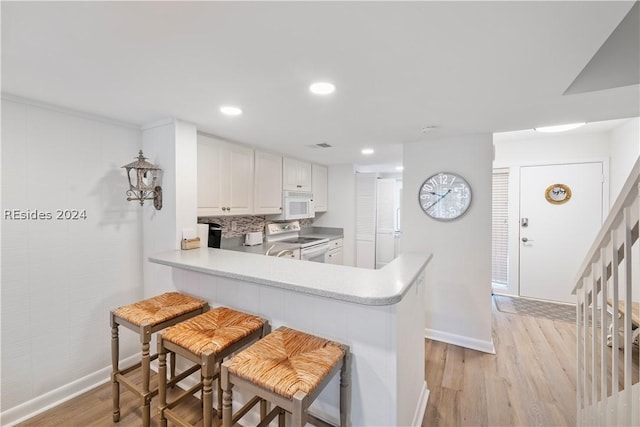 kitchen with white cabinetry, white appliances, light hardwood / wood-style floors, and kitchen peninsula