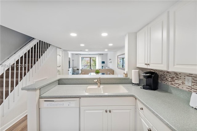 kitchen with tasteful backsplash, sink, white cabinets, white dishwasher, and kitchen peninsula