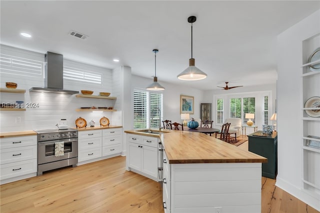 kitchen featuring butcher block counters, white cabinetry, a kitchen island, high end stove, and wall chimney range hood