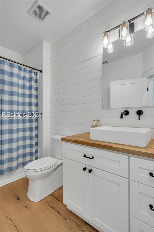 full bathroom with shower / tub combo with curtain, toilet, wood walls, wood-type flooring, and vanity