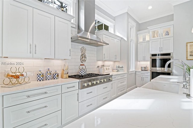 kitchen featuring white cabinetry, backsplash, stainless steel appliances, ventilation hood, and ornamental molding