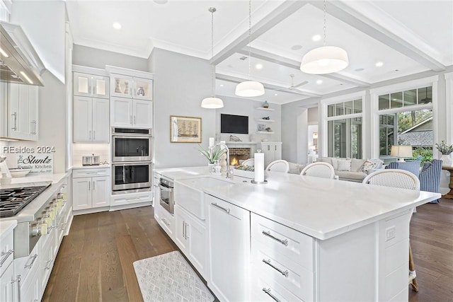 kitchen with wall chimney range hood, white cabinetry, a center island with sink, a kitchen bar, and decorative backsplash