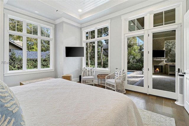 bedroom featuring a raised ceiling, crown molding, dark hardwood / wood-style floors, and access to exterior